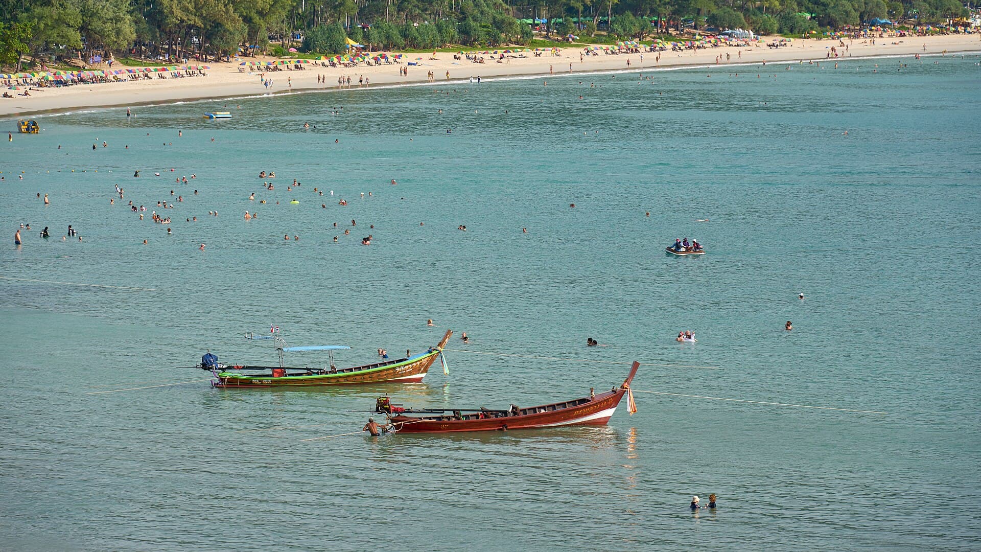 Longtail boats and swimmers in the turquoise water off Kata Beach